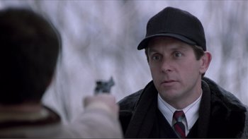 A man holding a gun pointed at another man in a hat