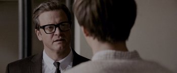 Movie still from “A Single Man” (2009), directed by Tom Ford – A man wearing a suit and tie talking to another man in front of a mirror; Close Up shot, Over the shoulder angle