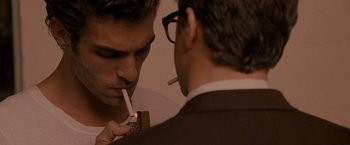 Movie still from “A Single Man” (2009), directed by Tom Ford – A man smoking a cigarette while another man holds a cell phone in his mouth; Close Up shot, Over the shoulder angle