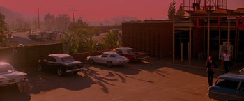 Movie still from “A Single Man” (2009), directed by Tom Ford – A parking lot filled with parked cars near a brick building; Extreme Wide shot, High angle