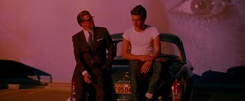 Movie still from “A Single Man” (2009), directed by Tom Ford – A man sitting on the back of a car next to another man; Medium shot, Over the shoulder angle