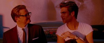 Movie still from “A Single Man” (2009), directed by Tom Ford – A man and a woman sitting next to each other in front of a car; Close Up shot, Over the shoulder angle