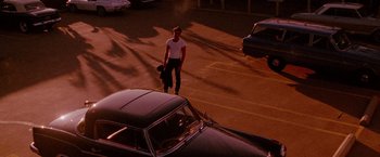 Movie still from “A Single Man” (2009), directed by Tom Ford – A man holding a skate board while standing in a parking lot; Wide shot, High angle
