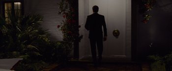 Movie still from “A Single Man” (2009), directed by Tom Ford – A man in a black suit is standing in front of a white door; Wide shot, Over the shoulder angle