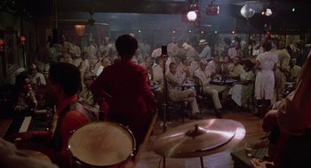 Movie still from “A Soldier's Story” (1984), directed by Norman Jewison – A group of people sitting in a room with drums; Extreme Wide shot, High angle