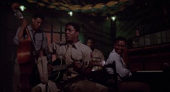 Movie still from “A Soldier's Story” (1984), directed by Norman Jewison – A group of men sitting around a table playing guitar; Medium shot, Low angle