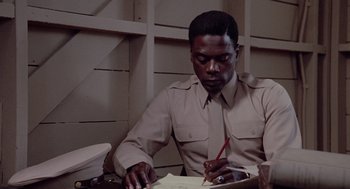 Movie still from “A Soldier's Story” (1984), directed by Norman Jewison – A man sitting at a table writing on a piece of paper; Close Up shot, Low angle