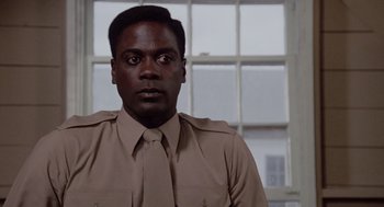 Movie still from “A Soldier's Story” (1984), directed by Norman Jewison – A man wearing a tan shirt and a tie in front of a window; Close Up shot, Low angle