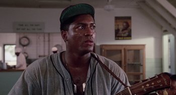 Movie still from “A Soldier's Story” (1984), directed by Norman Jewison – A person holding a guitar in a room; Close Up shot, Low angle