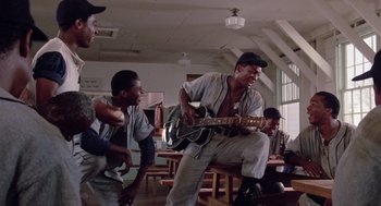 Movie still from “A Soldier's Story” (1984), directed by Norman Jewison – A group of men sitting in a room playing a guitar; Wide shot, Low angle