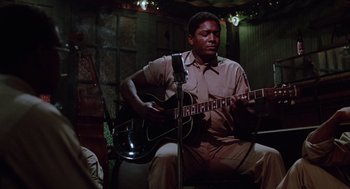 Movie still from “A Soldier's Story” (1984), directed by Norman Jewison – A man sitting down playing an electric guitar in front of a microphone; Medium shot, Low angle