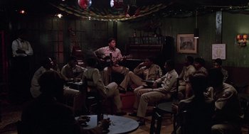 Movie still from “A Soldier's Story” (1984), directed by Norman Jewison – A group of men sitting around a living room playing guitar; Wide shot, High angle