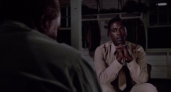 Movie still from “A Soldier's Story” (1984), directed by Norman Jewison – Two men are sitting in a room and one of them is holding his hands together; Medium shot, Over the shoulder angle