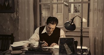Movie still from “A Special Day” (1977), directed by Ettore Scola – A man sitting at a desk writing on a piece of paper; Medium shot, High angle