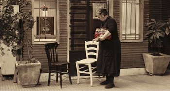 Movie still from “A Special Day” (1977), directed by Ettore Scola – An older woman is standing in front of a chair; Wide shot, High angle