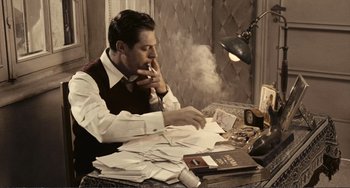 Movie still from “A Special Day” (1977), directed by Ettore Scola – A man sitting at a desk with papers and a cigarette; Medium shot, High angle