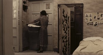 Movie still from “A Special Day” (1977), directed by Ettore Scola – A woman in a dress standing in front of an open door; Wide shot, High angle