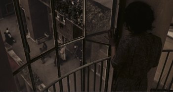 Movie still from “A Special Day” (1977), directed by Ettore Scola – A person standing on top of an iron railing looking out of a window; Extreme Wide shot, High angle