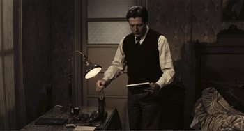Movie still from “A Special Day” (1977), directed by Ettore Scola – A man standing in front of a table with a lamp on top of it; Medium shot, Low angle