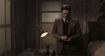 Movie still from “A Special Day” (1977), directed by Ettore Scola – A man in a suit and tie standing in front of a lamp; Medium shot, Low angle