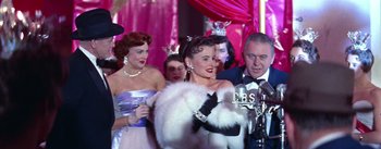 Movie still from “A Star Is Born” (1954), directed by George Cukor – A group of people in a room next to a microphone; Medium shot, Low angle