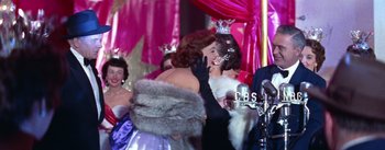 Movie still from “A Star Is Born” (1954), directed by George Cukor – A woman in a white dress and a fur coat is talking to another woman in a black dress and a fur coat; Medium shot, Over the shoulder angle