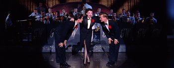 Movie still from “A Star Is Born” (1954), directed by George Cukor – A group of men and a woman on a stage; Wide shot, High angle