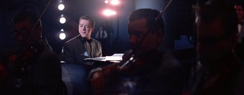 Movie still from “A Star Is Born” (1954), directed by George Cukor – A man is playing a violin while another man looks on; Medium shot, Low angle
