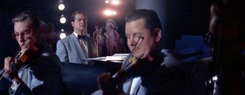 Movie still from “A Star Is Born” (1954), directed by George Cukor – A man playing a violin in front of a crowd; Medium shot, Low angle