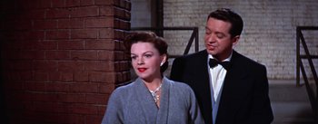 Movie still from “A Star Is Born” (1954), directed by George Cukor – An older woman and a younger man standing next to a brick wall; Medium shot, Over the shoulder angle