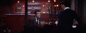 Movie still from “A Star Is Born” (1954), directed by George Cukor – A man sitting at a table in front of a glass of whiskey; Medium shot, Over the shoulder angle