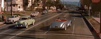 Movie still from “A Star Is Born” (1954), directed by George Cukor – An old car driving down a street past palm trees; Extreme Wide shot, High angle