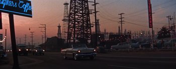 Movie still from “A Star Is Born” (1954), directed by George Cukor – A car driving down a street next to power lines; Extreme Wide shot, High angle