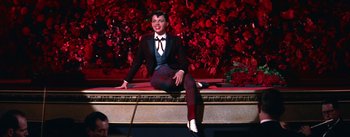 Movie still from “A Star Is Born” (1954), directed by George Cukor – A woman sitting on top of a bench in front of a wall of flowers; Wide shot, Low angle