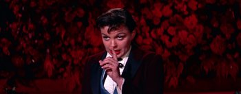 Movie still from “A Star Is Born” (1954), directed by George Cukor – A woman in a suit and tie holding her finger to her mouth; Close Up shot, High angle