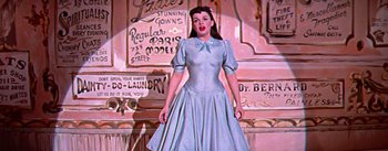 Movie still from “A Star Is Born” (1954), directed by George Cukor – A woman in a blue dress standing in front of a building; Medium shot, Low angle