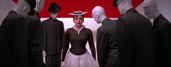 Movie still from “A Star Is Born” (1954), directed by George Cukor – A woman in a black dress and a hat standing in front of two men in black suits; Medium shot, Low angle