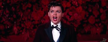 Movie still from “A Star Is Born” (1954), directed by George Cukor – A woman wearing a suit and a bow tie; Close Up shot, Low angle