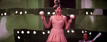 Movie still from “A Star Is Born” (1954), directed by George Cukor – A woman in a pink dress holding two white balls; Medium shot, Low angle
