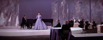 Movie still from “A Star Is Born” (1954), directed by George Cukor – A woman in a blue dress standing in front of a piano; Wide shot, High angle