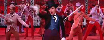 Movie still from “A Star Is Born” (1954), directed by George Cukor – A woman wearing a top hat and holding a whip; Medium shot, Low angle