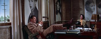 Movie still from “A Star Is Born” (1954), directed by George Cukor – A man sitting on a chair in front of a window; Wide shot, Low angle