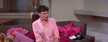Movie still from “A Star Is Born” (1954), directed by George Cukor – A woman sitting on a bed wearing a pink shirt; Medium shot, Over the shoulder angle
