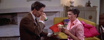 Movie still from “A Star Is Born” (1954), directed by George Cukor – A man and a woman are eating and drinking; Medium shot, High angle