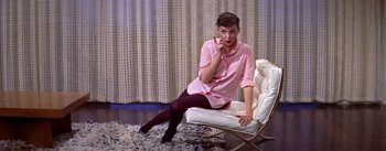 Movie still from “A Star Is Born” (1954), directed by George Cukor – A woman sitting on top of a chair in a living room; Wide shot, High angle