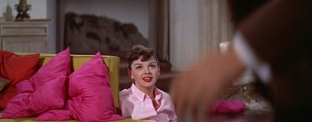 Movie still from “A Star Is Born” (1954), directed by George Cukor – A woman sitting in a chair wearing a pink shirt; Medium shot, Over the shoulder angle
