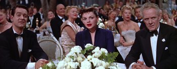 Movie still from “A Star Is Born” (1954), directed by George Cukor – A woman sitting in front of a table with flowers; Medium shot, Over the shoulder angle