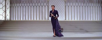 Movie still from “A Star Is Born” (1954), directed by George Cukor – A woman in a purple dress holding a gold trophy; Wide shot, Low angle