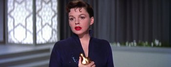 Movie still from “A Star Is Born” (1954), directed by George Cukor – A woman holding a golden object in her hand; Close Up shot, Low angle