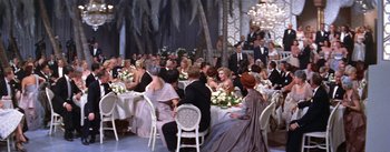 Movie still from “A Star Is Born” (1954), directed by George Cukor – A group of people sitting around a table at an event; Extreme Wide shot, High angle